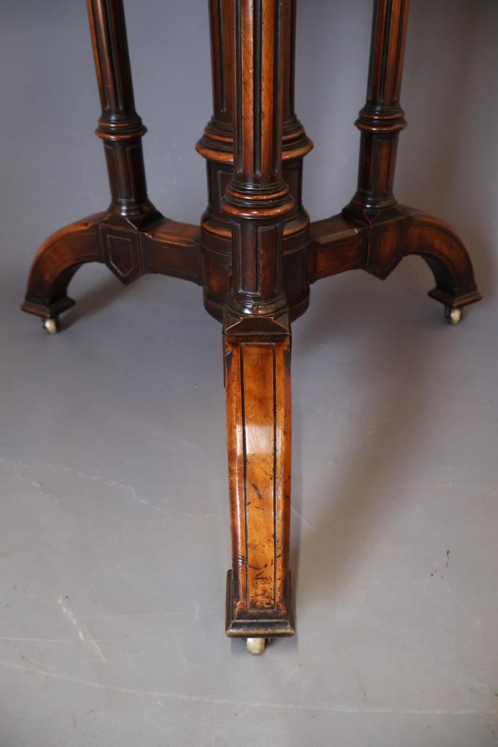 A circular burr walnut centre table featuring a figured top, turned central pedestal, four outer colonnettes, and splayed legs on castors. View III