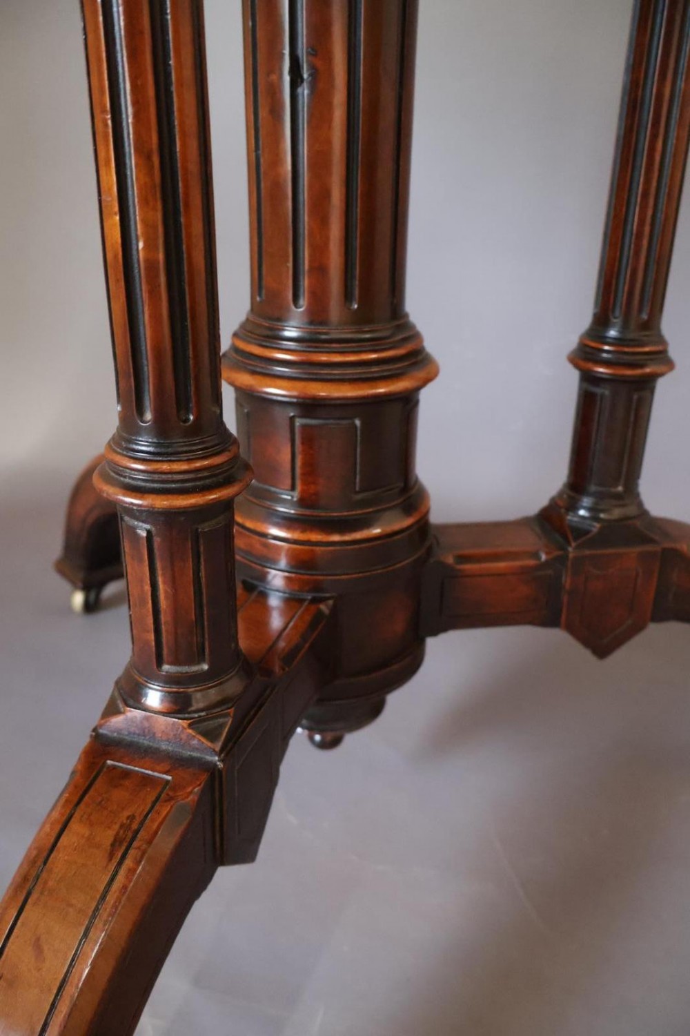 A circular burr walnut centre table featuring a figured top, turned central pedestal, four outer colonnettes, and splayed legs on castors. View IV
