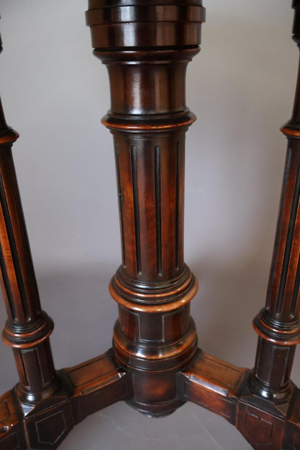 A circular burr walnut centre table featuring a figured top, turned central pedestal, four outer colonnettes, and splayed legs on castors. View V