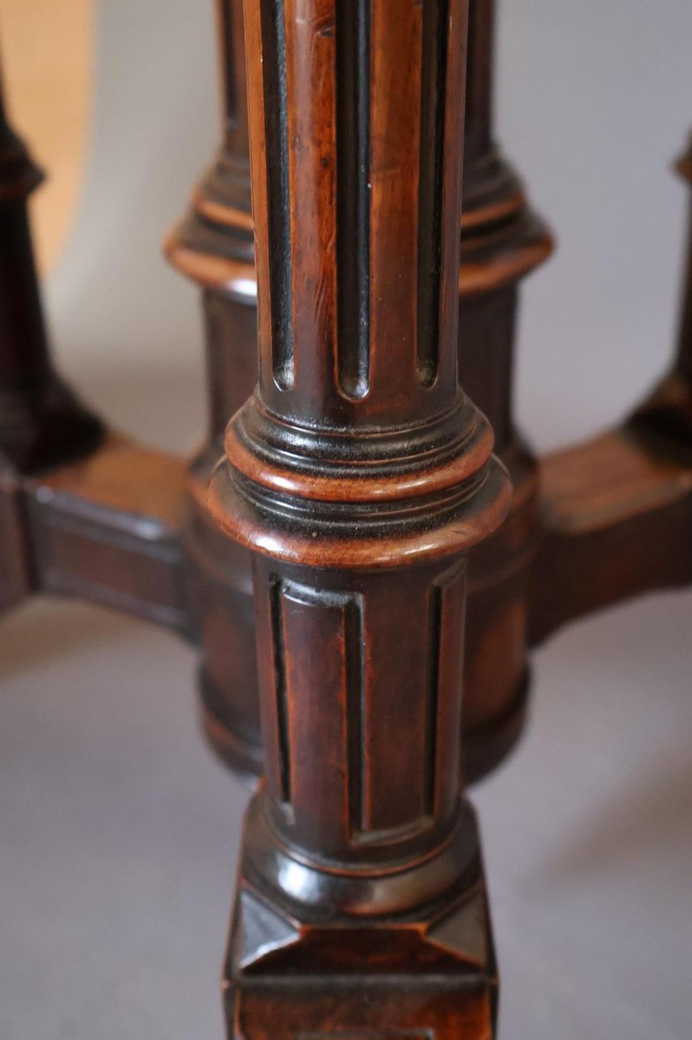 A circular burr walnut centre table featuring a figured top, turned central pedestal, four outer colonnettes, and splayed legs on castors. View VI