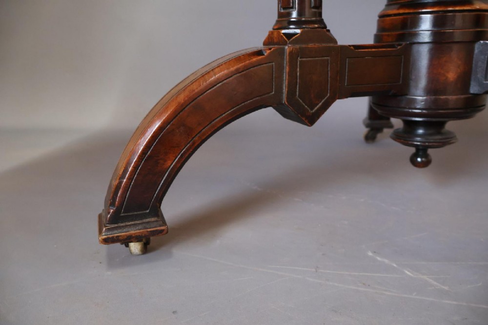 A circular burr walnut centre table featuring a figured top, turned central pedestal, four outer colonnettes, and splayed legs on castors. View VII
