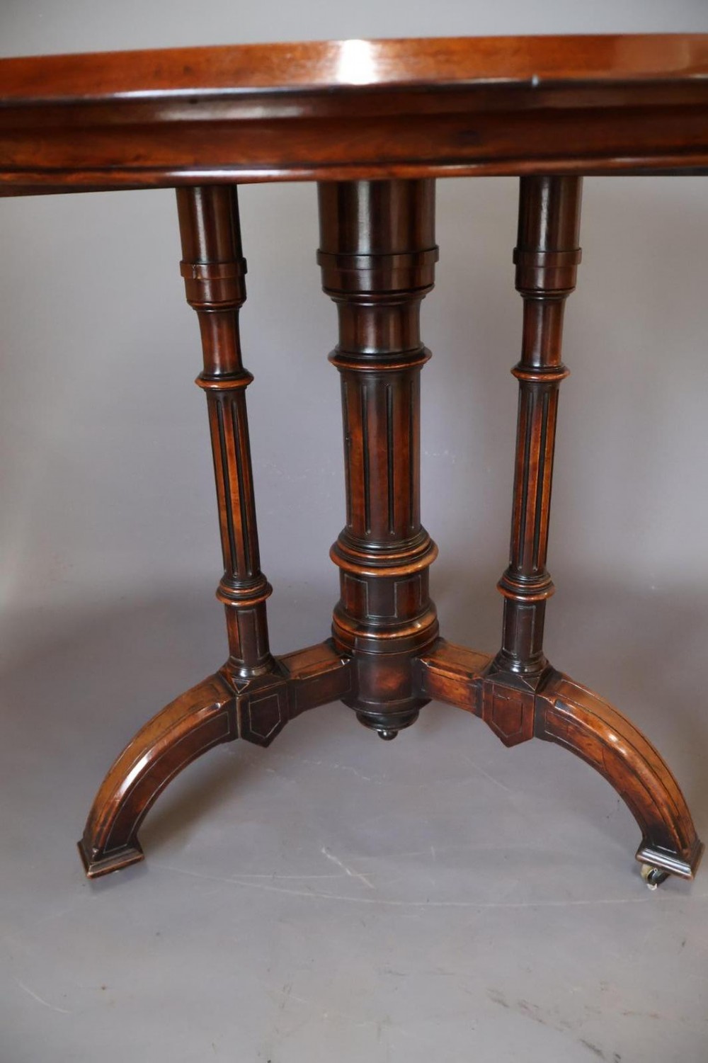 A circular burr walnut centre table featuring a figured top, turned central pedestal, four outer colonnettes, and splayed legs on castors. View VIII