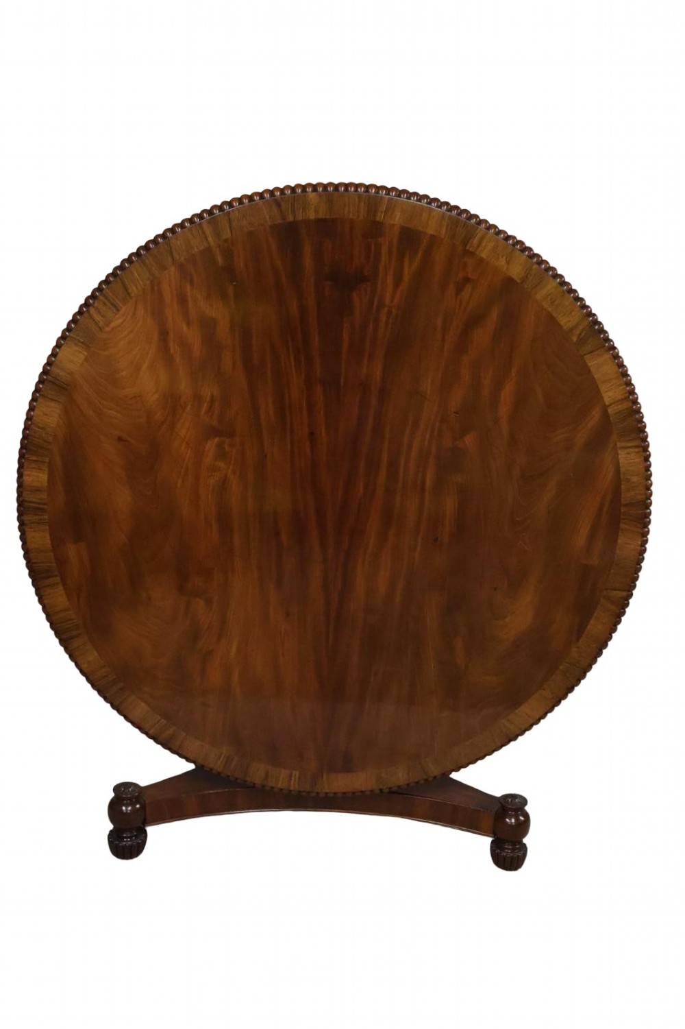 A Regency circular flame mahogany centre table shown in a tilted position on a curved triform base.
