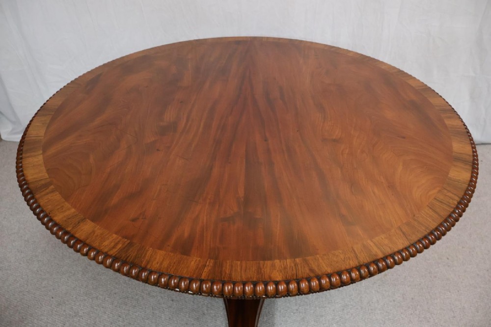 A Regency circular flame mahogany centre table shown in a tilted position on a curved triform base. View IV