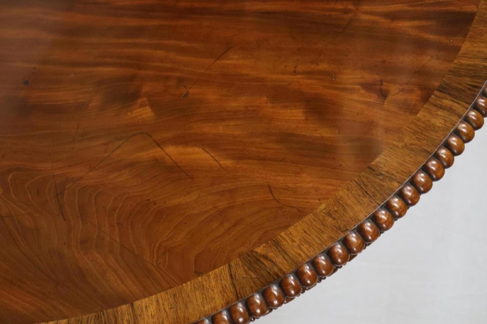 A Regency circular flame mahogany centre table shown in a tilted position on a curved triform base. View V
