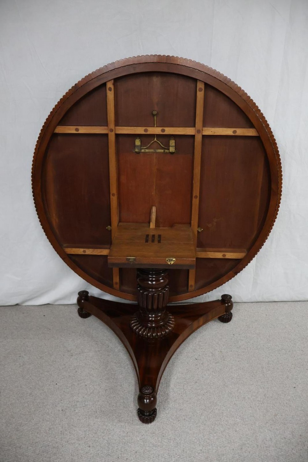 A Regency circular flame mahogany centre table shown in a tilted position on a curved triform base. View VIII