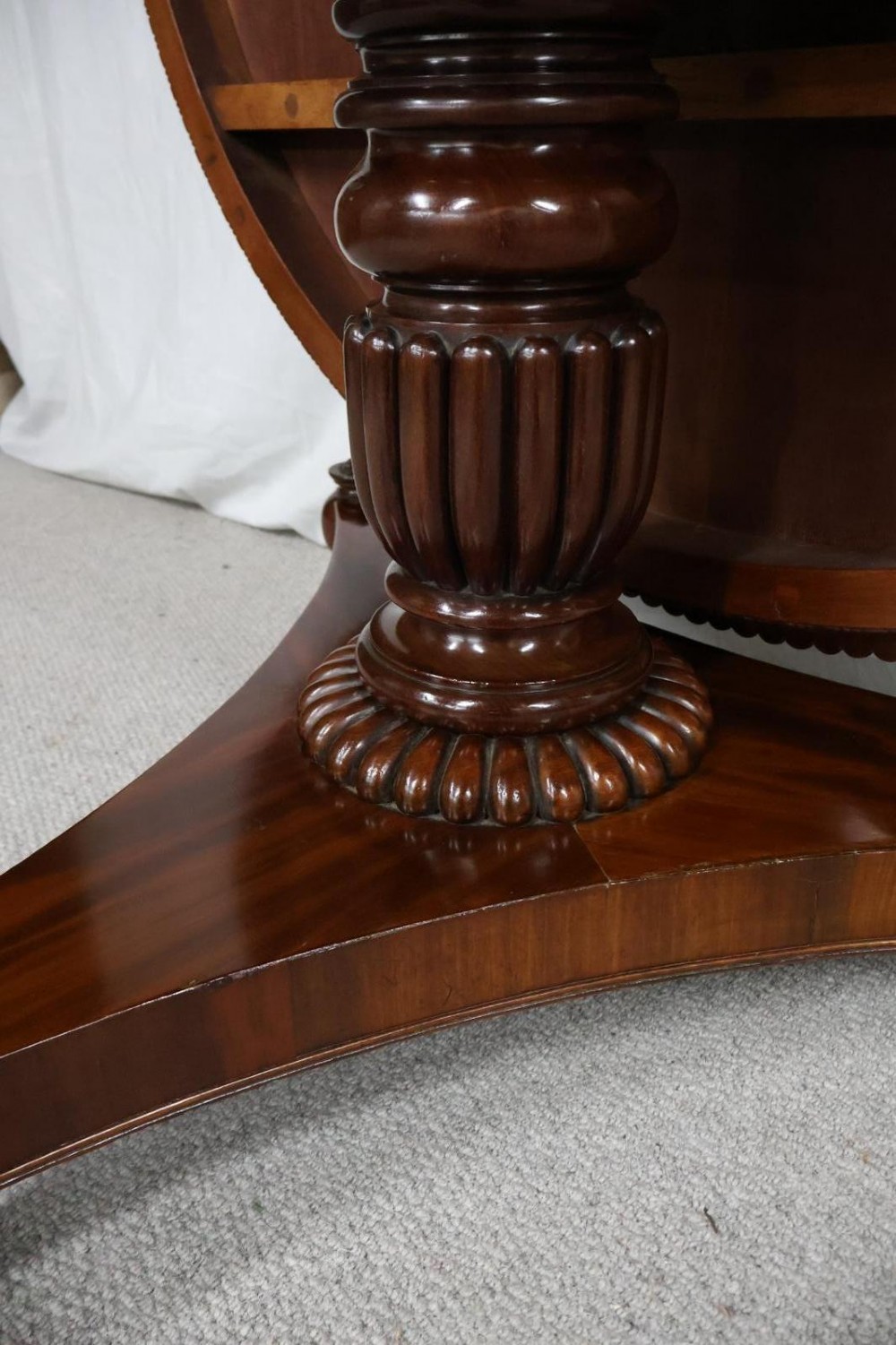 A Regency circular flame mahogany centre table shown in a tilted position on a curved triform base. View XI