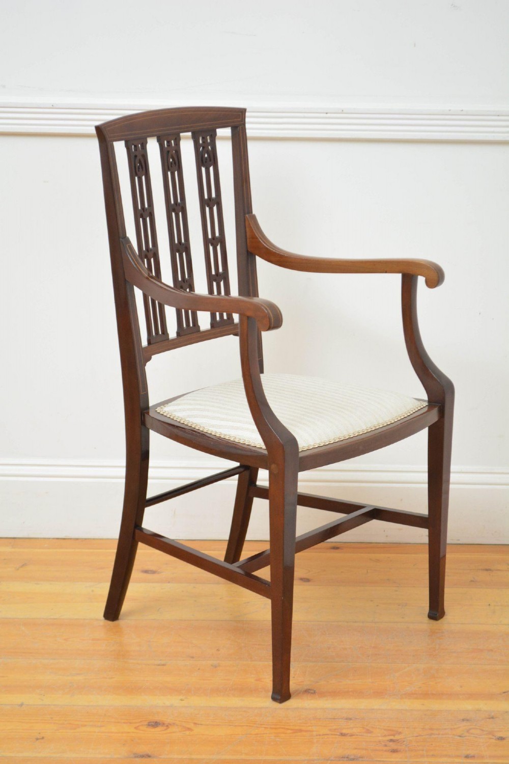 An Art Nouveau mahogany armchair featuring a pierced back splat with inlaid detailing, swept armrests, and a cream striped upholstered seat.