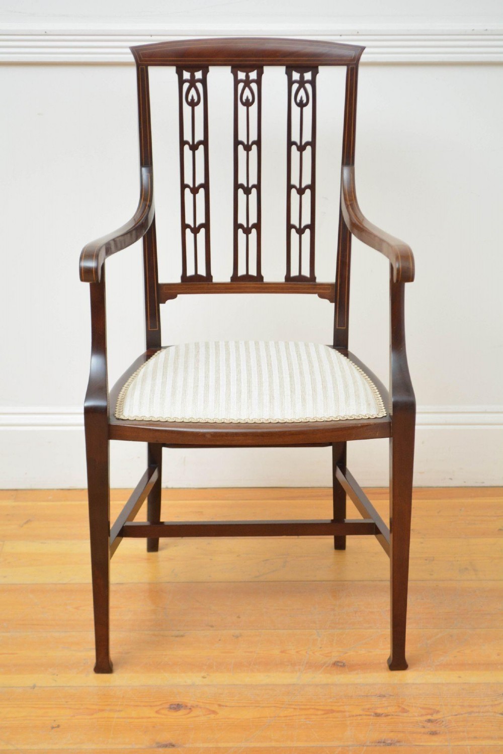 An Art Nouveau mahogany armchair featuring a pierced back splat with inlaid detailing, swept armrests, and a cream striped upholstered seat. View IV
