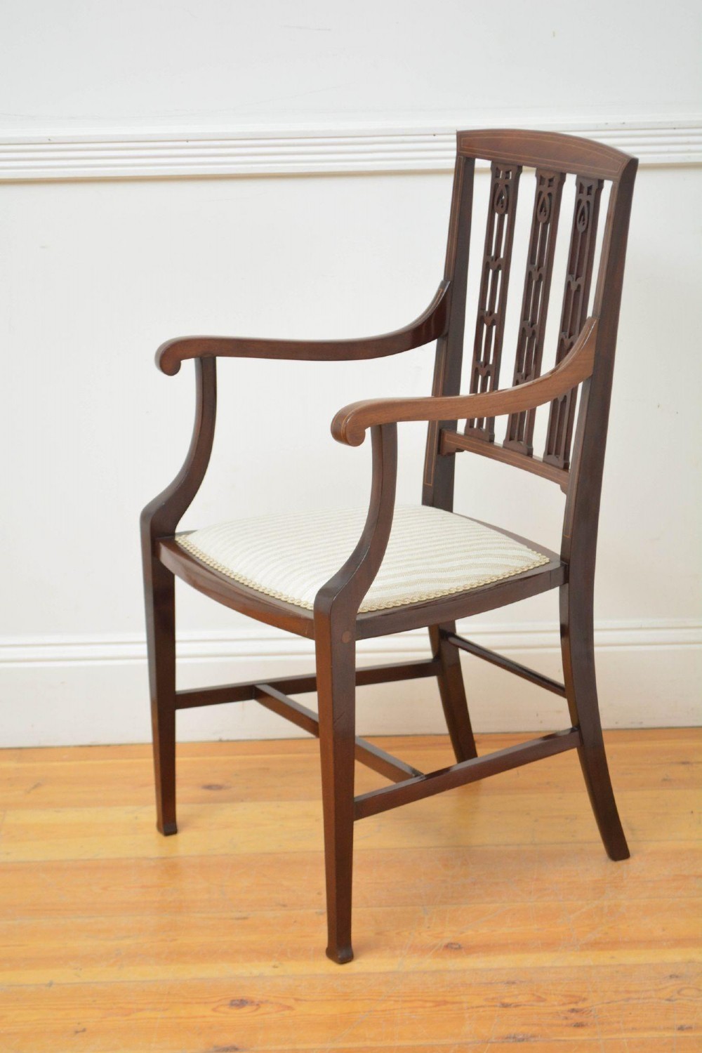 An Art Nouveau mahogany armchair featuring a pierced back splat with inlaid detailing, swept armrests, and a cream striped upholstered seat. View V