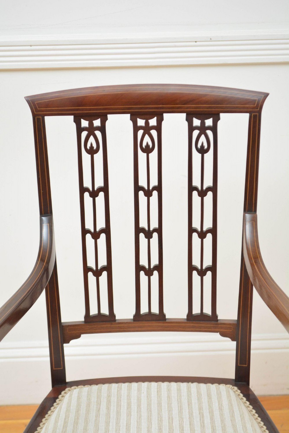 An Art Nouveau mahogany armchair featuring a pierced back splat with inlaid detailing, swept armrests, and a cream striped upholstered seat. View VI
