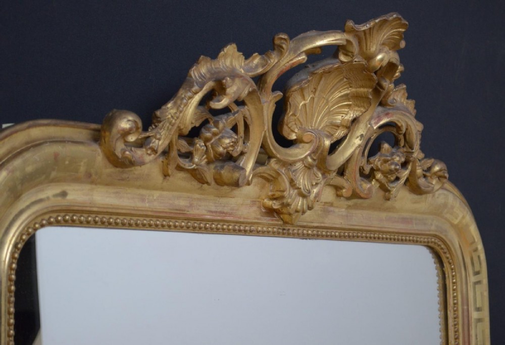 A 19th-century French wall mirror featuring a rectangular frame with rounded top corners, a gold leaf finish, and an ornate carved shell cresting. View II