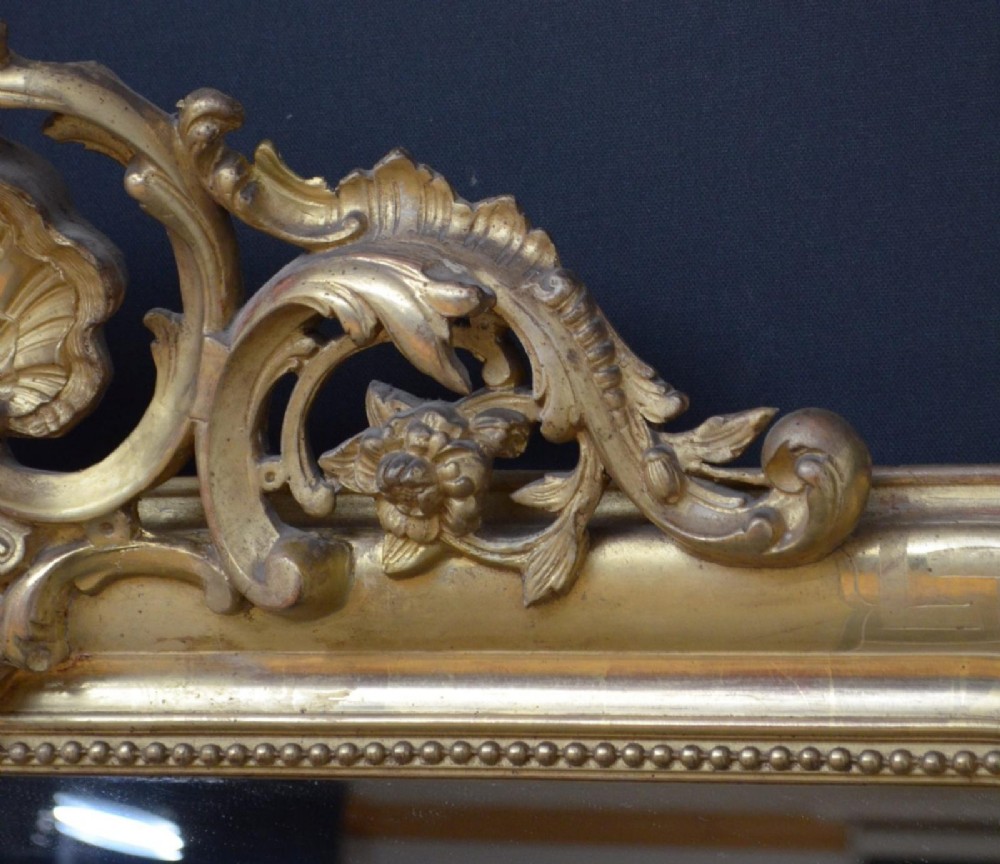 A 19th-century French wall mirror featuring a rectangular frame with rounded top corners, a gold leaf finish, and an ornate carved shell cresting. View V