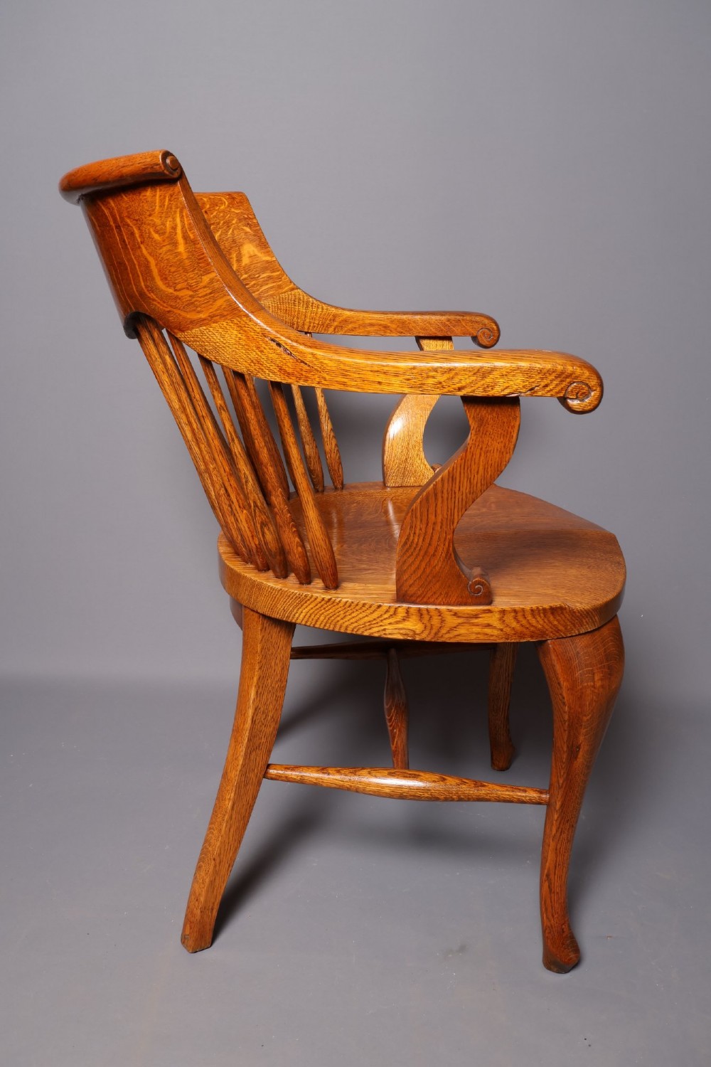 An antique Victorian golden oak desk chair featuring a curved spindle back, curved armrests, a contoured seat, and cabriole front legs. View II