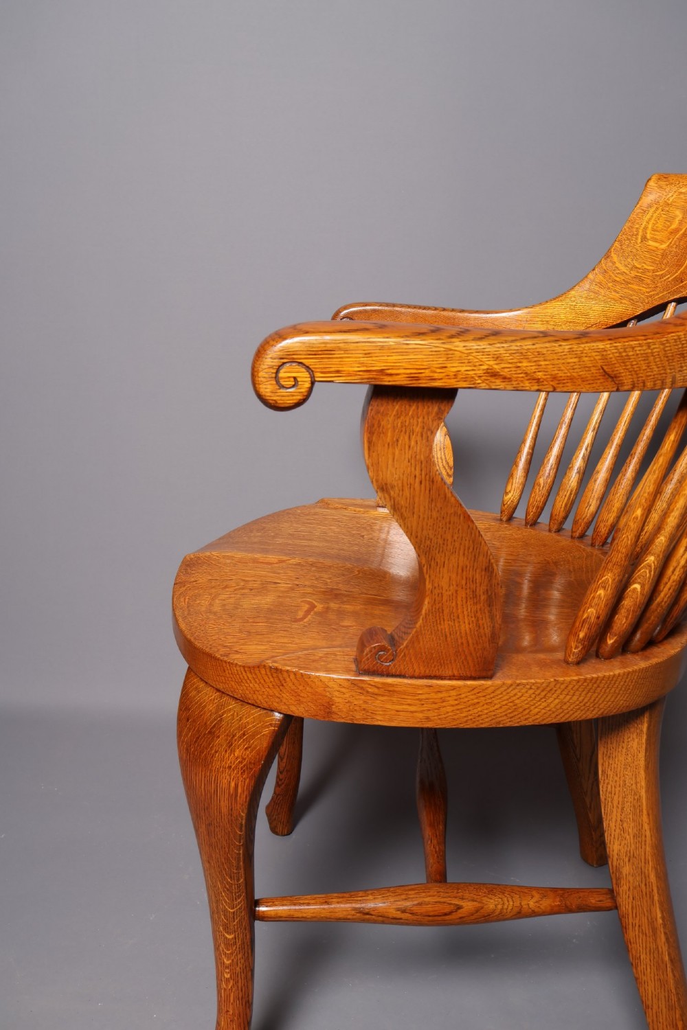 An antique Victorian golden oak desk chair featuring a curved spindle back, curved armrests, a contoured seat, and cabriole front legs. View IV