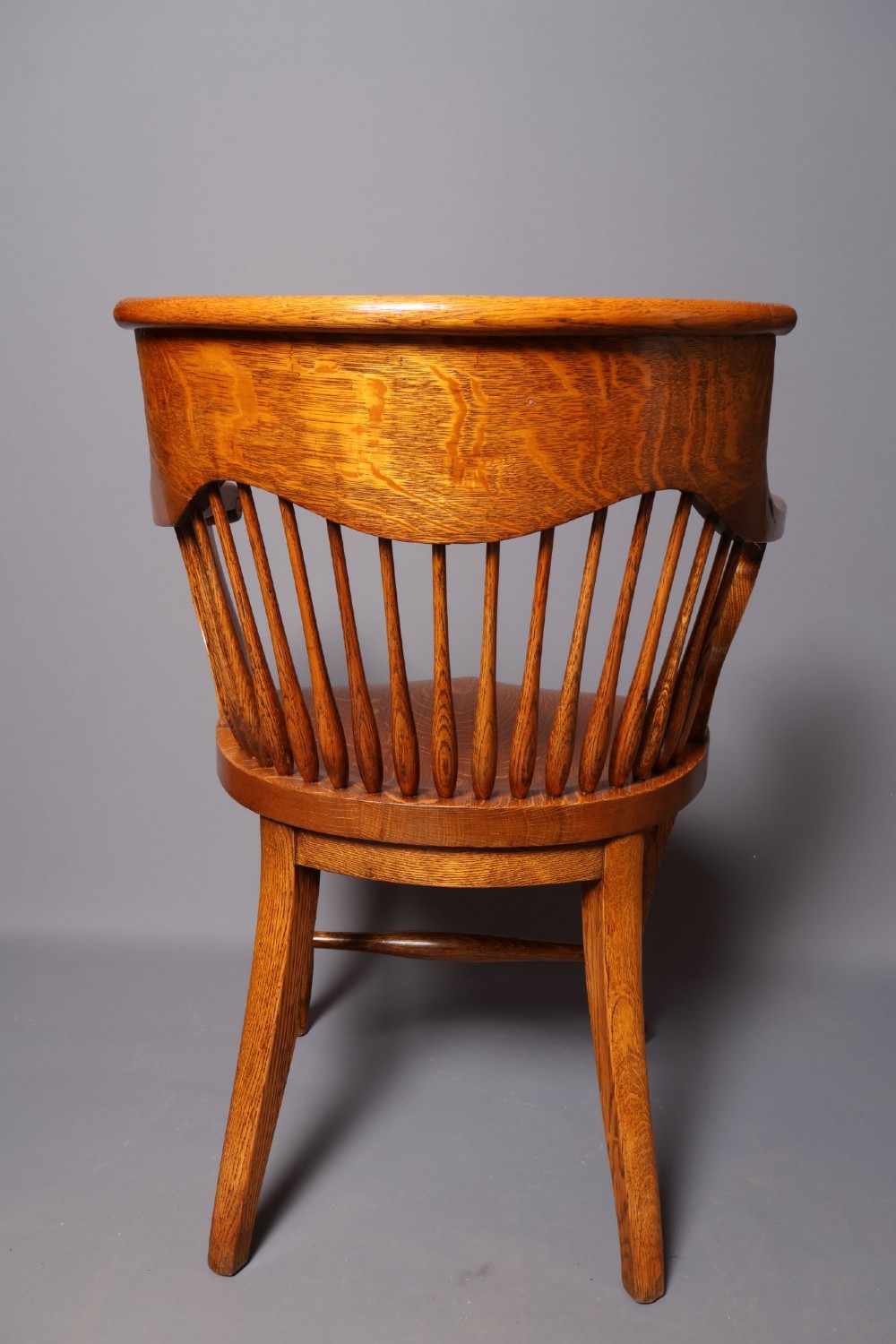 An antique Victorian golden oak desk chair featuring a curved spindle back, curved armrests, a contoured seat, and cabriole front legs. View V