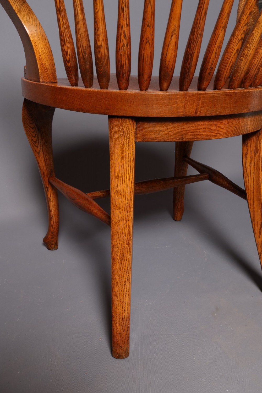 An antique Victorian golden oak desk chair featuring a curved spindle back, curved armrests, a contoured seat, and cabriole front legs. View VI