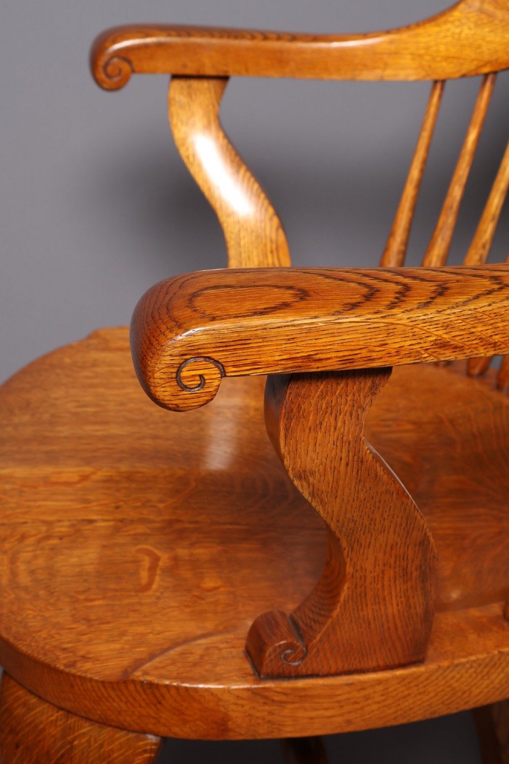An antique Victorian golden oak desk chair featuring a curved spindle back, curved armrests, a contoured seat, and cabriole front legs. View X
