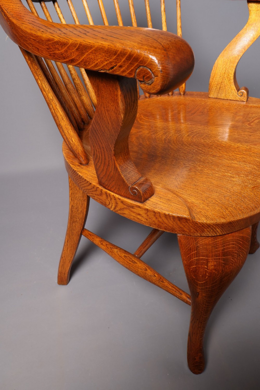An antique Victorian golden oak desk chair featuring a curved spindle back, curved armrests, a contoured seat, and cabriole front legs. View XIII