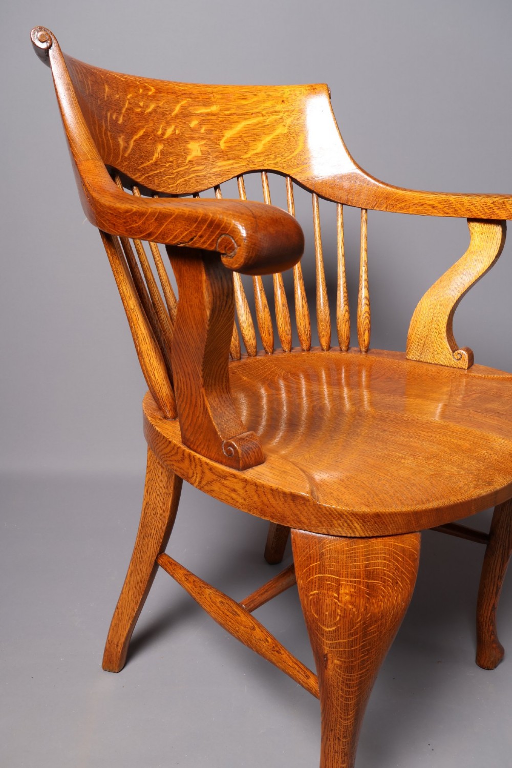 An antique Victorian golden oak desk chair featuring a curved spindle back, curved armrests, a contoured seat, and cabriole front legs. View XIV