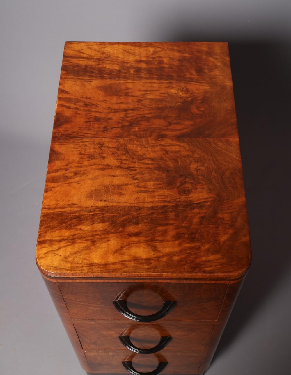 A matching pair of tall Art Deco burr walnut bedside cabinets with three drawers, dark curved handles, and ebonised plinth bases. View IV