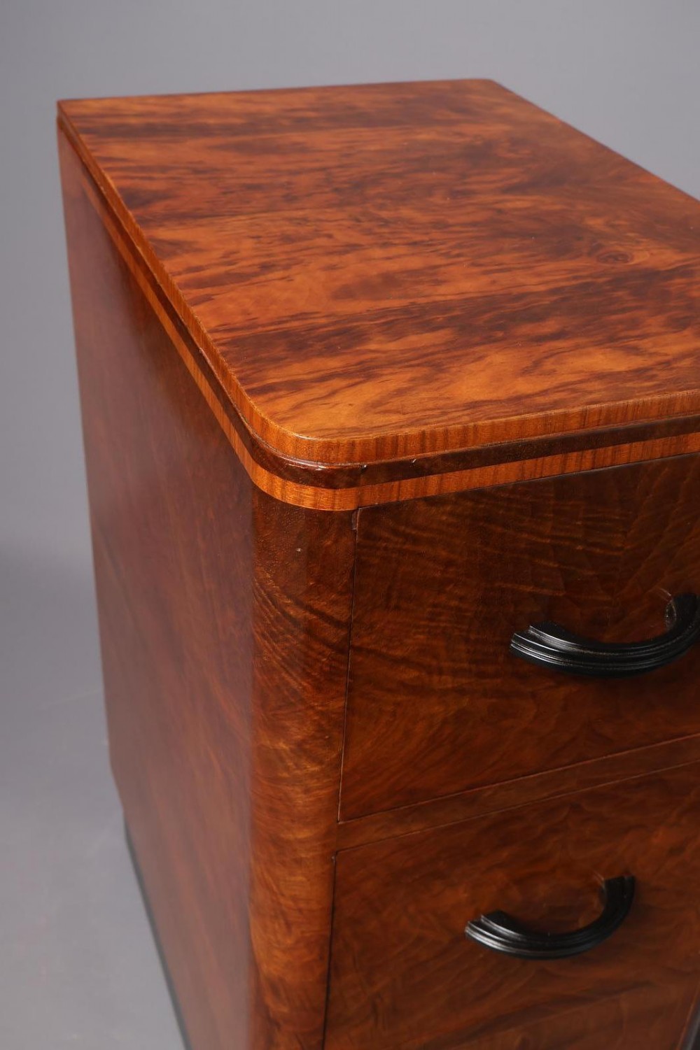 A matching pair of tall Art Deco burr walnut bedside cabinets with three drawers, dark curved handles, and ebonised plinth bases. View V