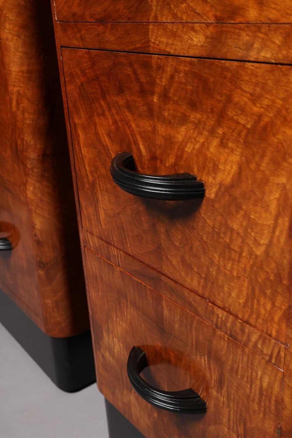 A matching pair of tall Art Deco burr walnut bedside cabinets with three drawers, dark curved handles, and ebonised plinth bases. View VIII