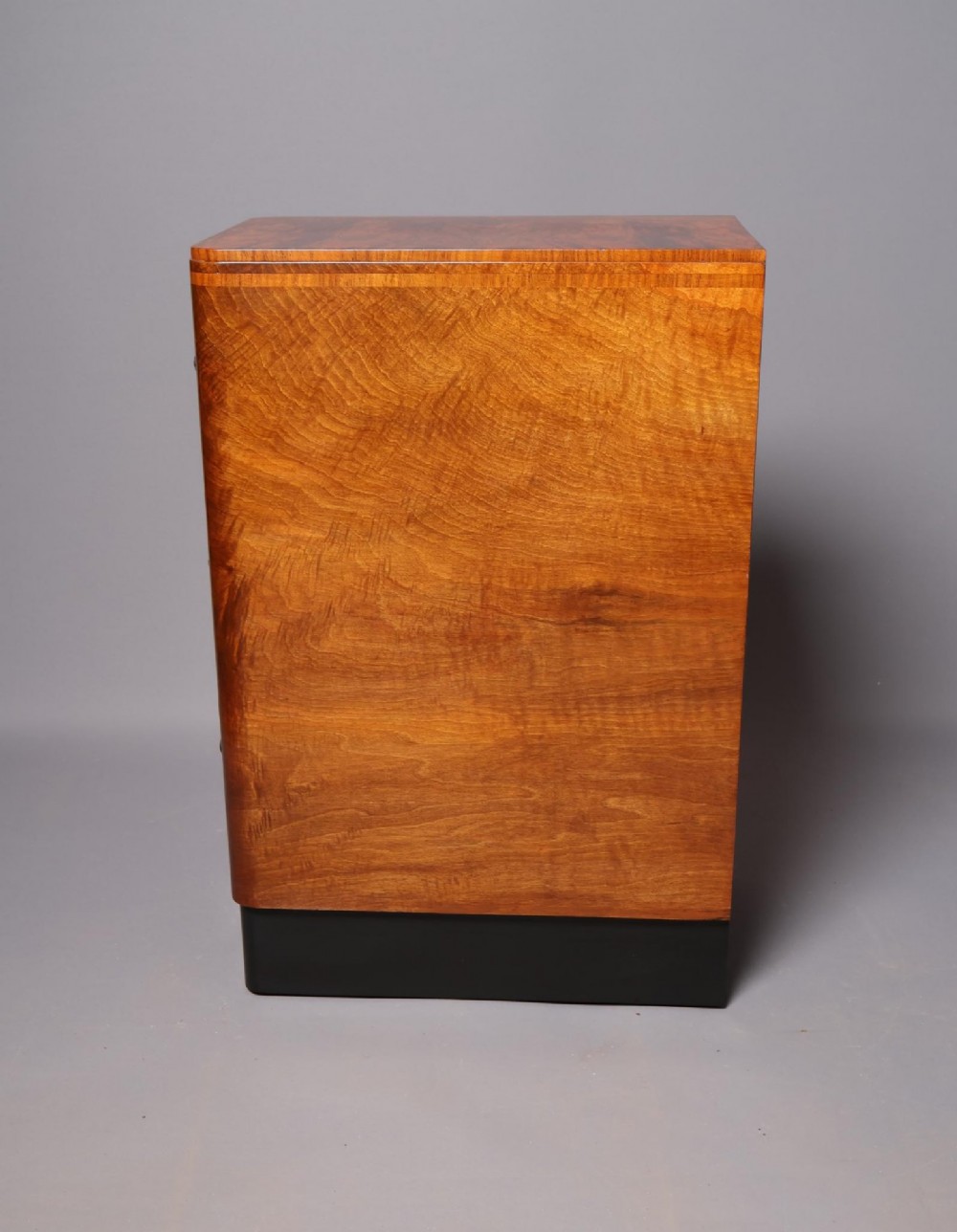A matching pair of tall Art Deco burr walnut bedside cabinets with three drawers, dark curved handles, and ebonised plinth bases. View X