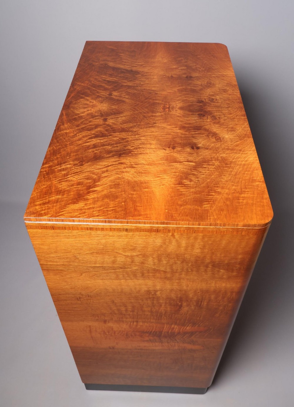 An Art Deco burr walnut compactum wardrobe featuring upper double doors, two long lower drawers, black curved handles, and an ebonised plinth. View III