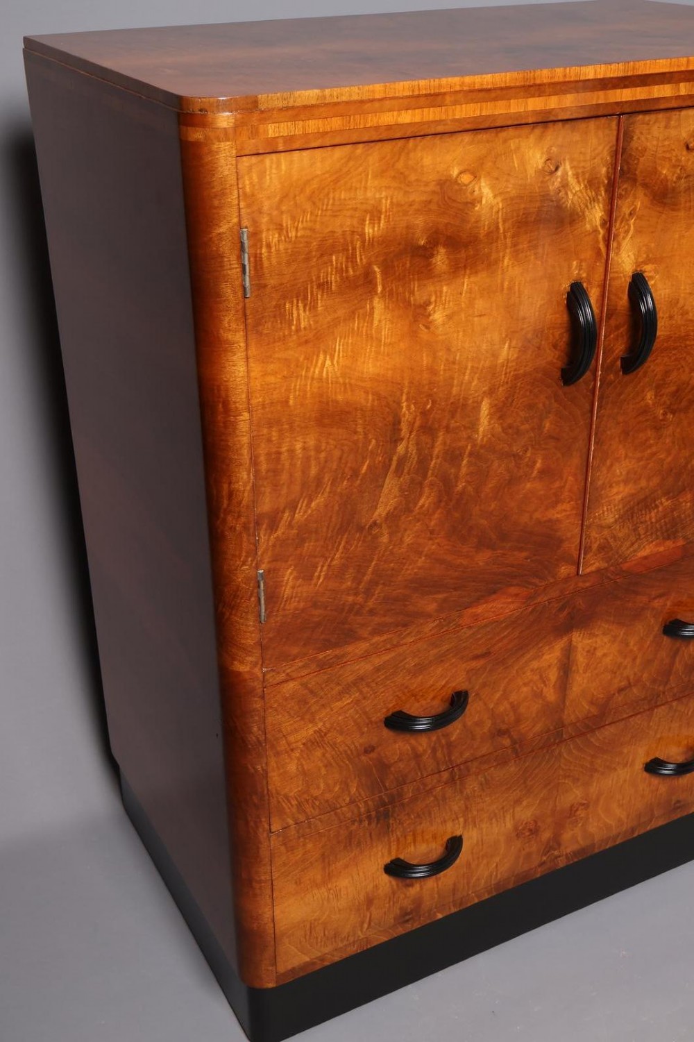 An Art Deco burr walnut compactum wardrobe featuring upper double doors, two long lower drawers, black curved handles, and an ebonised plinth. View V
