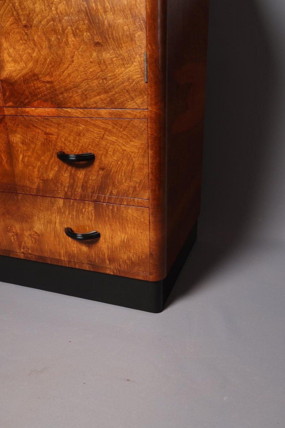 An Art Deco burr walnut compactum wardrobe featuring upper double doors, two long lower drawers, black curved handles, and an ebonised plinth. View VII