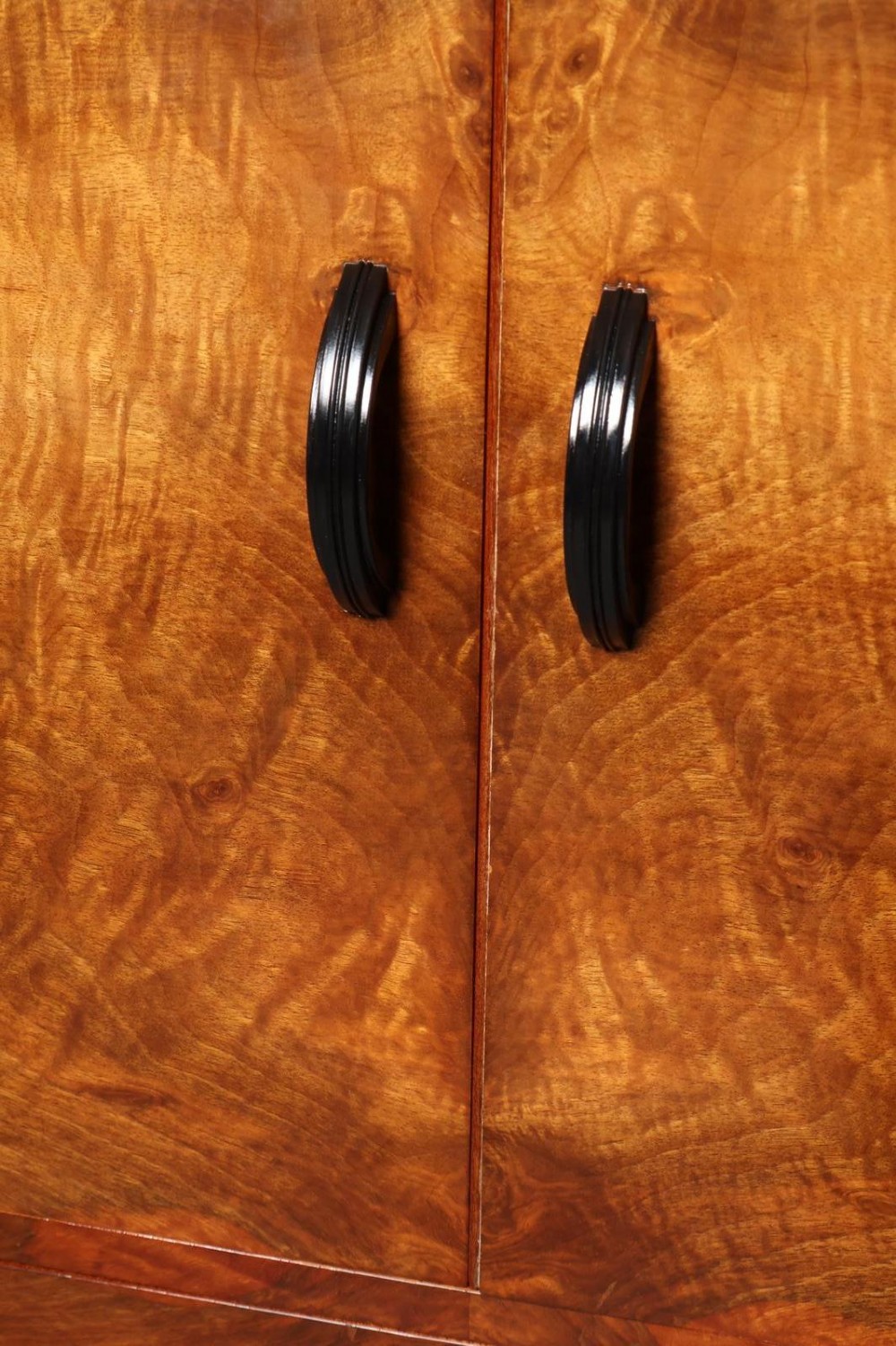 An Art Deco burr walnut compactum wardrobe featuring upper double doors, two long lower drawers, black curved handles, and an ebonised plinth. View VIII