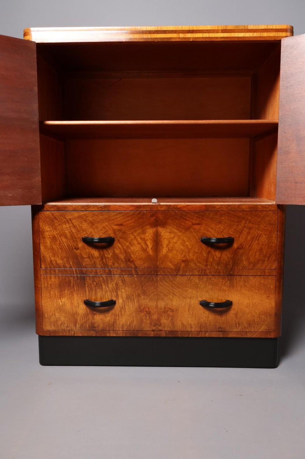 An Art Deco burr walnut compactum wardrobe featuring upper double doors, two long lower drawers, black curved handles, and an ebonised plinth. View IX
