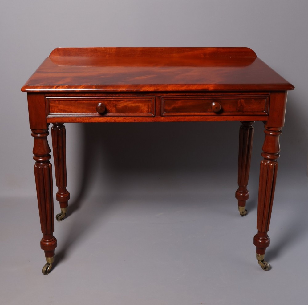 A Victorian mahogany writing table with a low gallery back, two frieze drawers with wooden knob handles, and turned reeded legs on brass castors.