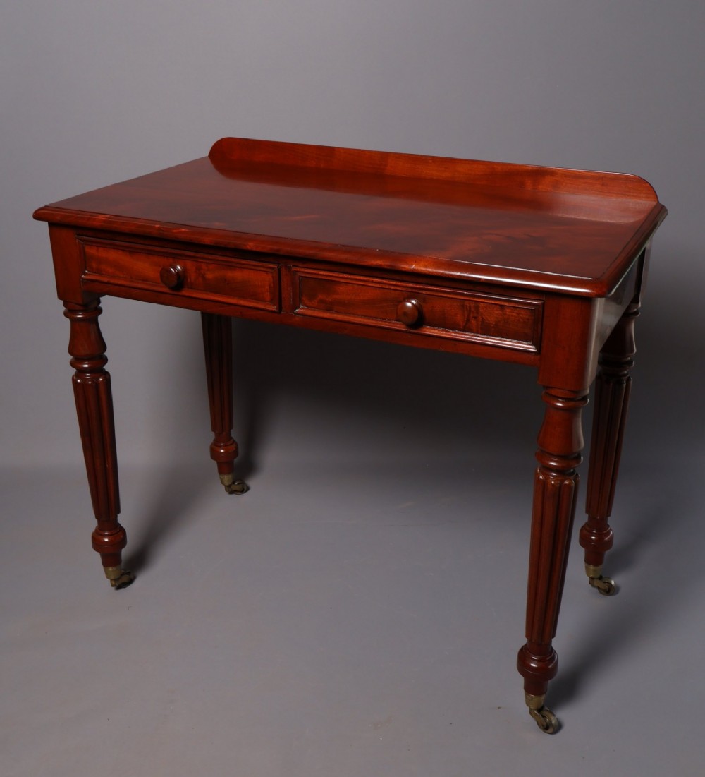 A Victorian mahogany writing table with a low gallery back, two frieze drawers with wooden knob handles, and turned reeded legs on brass castors. View III