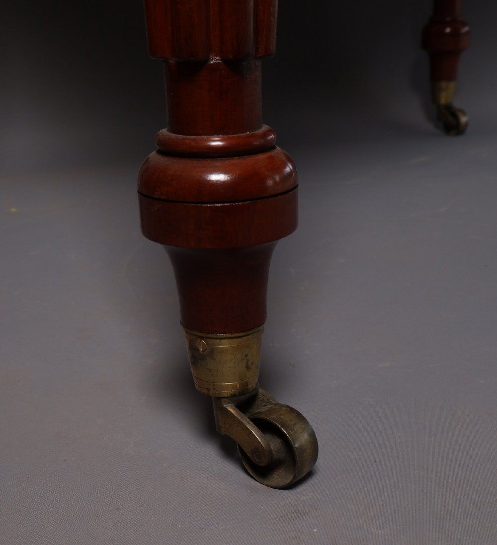 A Victorian mahogany writing table with a low gallery back, two frieze drawers with wooden knob handles, and turned reeded legs on brass castors. View V