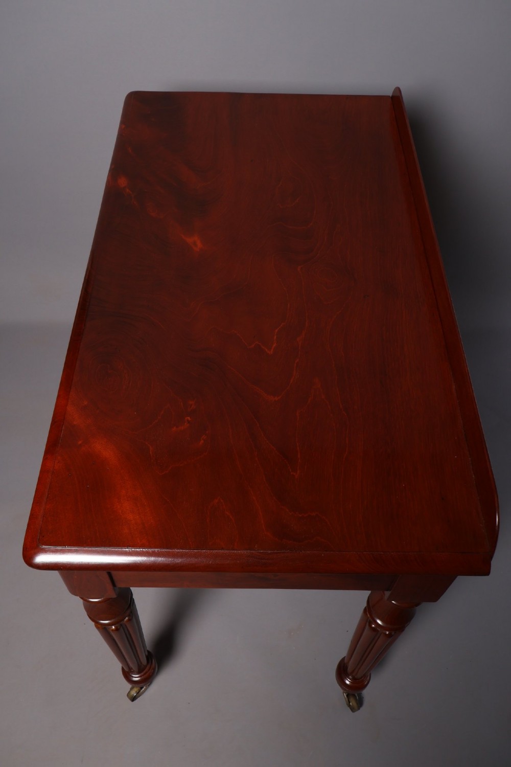 A Victorian mahogany writing table with a low gallery back, two frieze drawers with wooden knob handles, and turned reeded legs on brass castors. View VII
