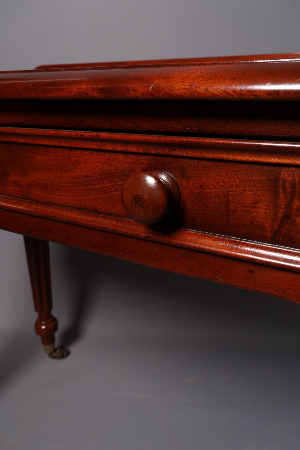 A Victorian mahogany writing table with a low gallery back, two frieze drawers with wooden knob handles, and turned reeded legs on brass castors. View IX