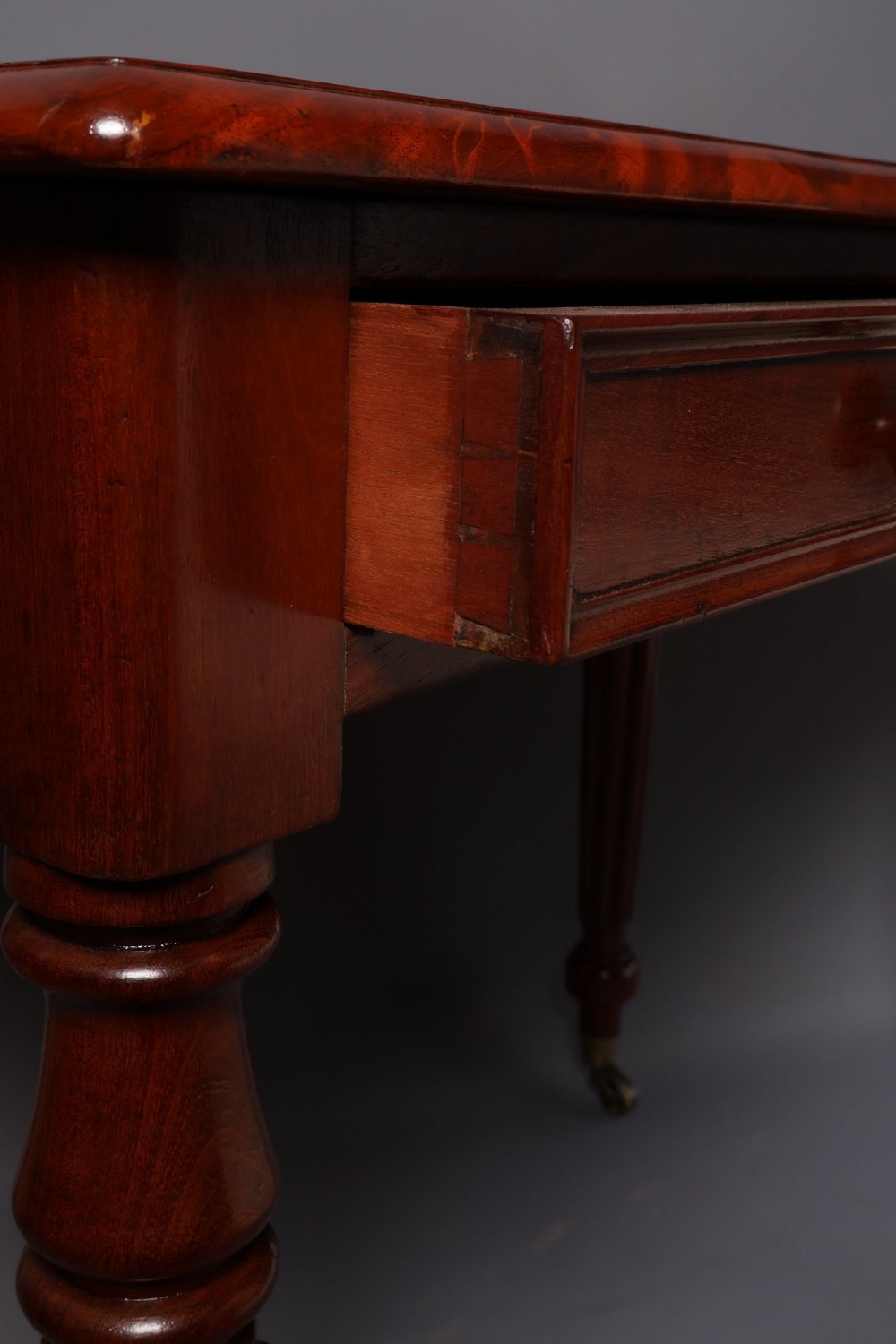 A Victorian mahogany writing table with a low gallery back, two frieze drawers with wooden knob handles, and turned reeded legs on brass castors. View X