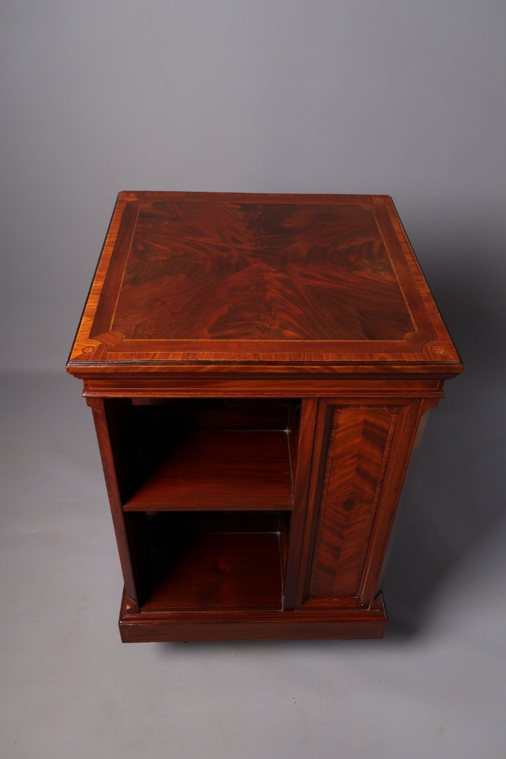 An Edwardian mahogany revolving bookcase featuring fine line inlay, flame-veneered vertical side panels, two shelving tiers, and a quadruped base with brass castors. View III