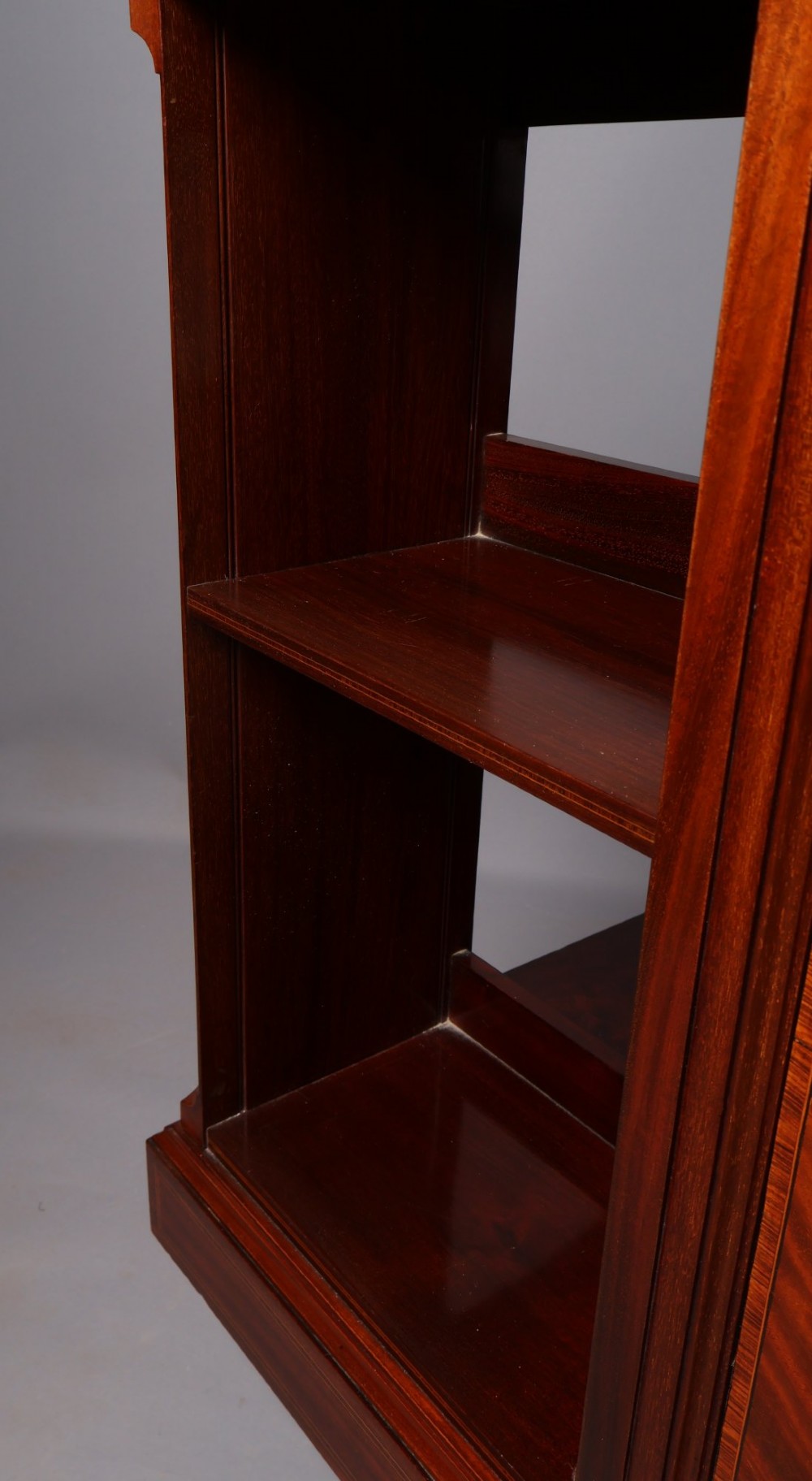 An Edwardian mahogany revolving bookcase featuring fine line inlay, flame-veneered vertical side panels, two shelving tiers, and a quadruped base with brass castors. View IV
