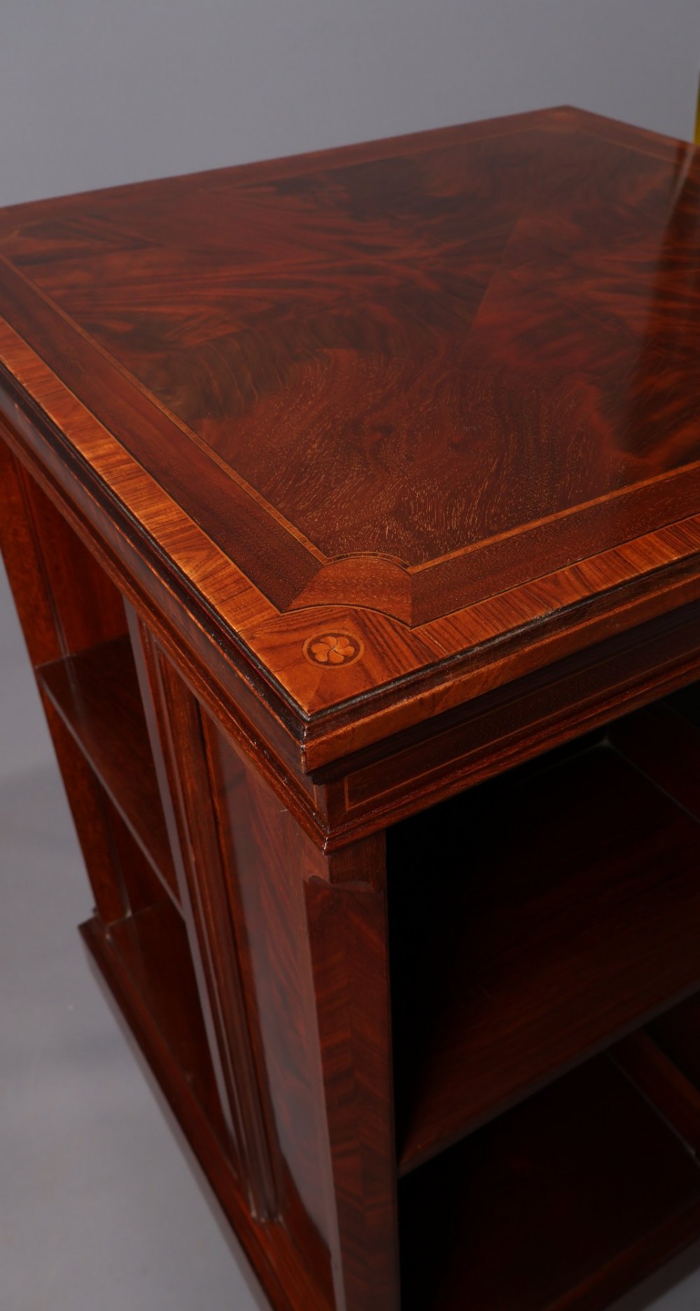 An Edwardian mahogany revolving bookcase featuring fine line inlay, flame-veneered vertical side panels, two shelving tiers, and a quadruped base with brass castors. View VIII