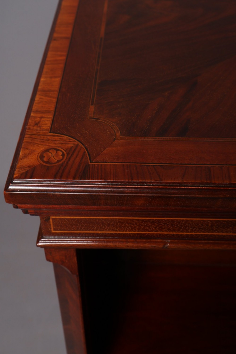 An Edwardian mahogany revolving bookcase featuring fine line inlay, flame-veneered vertical side panels, two shelving tiers, and a quadruped base with brass castors. View X