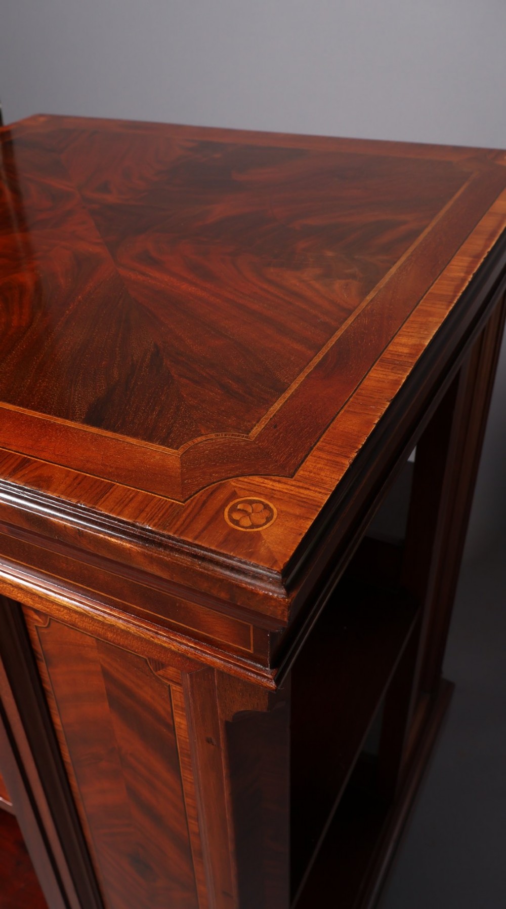 An Edwardian mahogany revolving bookcase featuring fine line inlay, flame-veneered vertical side panels, two shelving tiers, and a quadruped base with brass castors. View XI