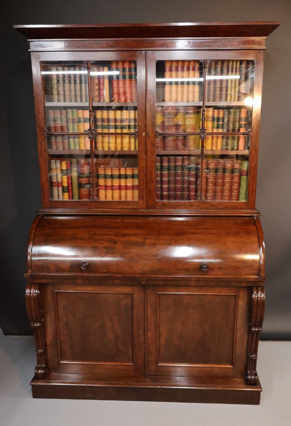 A William IV mahogany cylinder bureau bookcase featuring a two-door glazed upper cabinet, a rounded cylinder writing section, and lower cabinet doors.