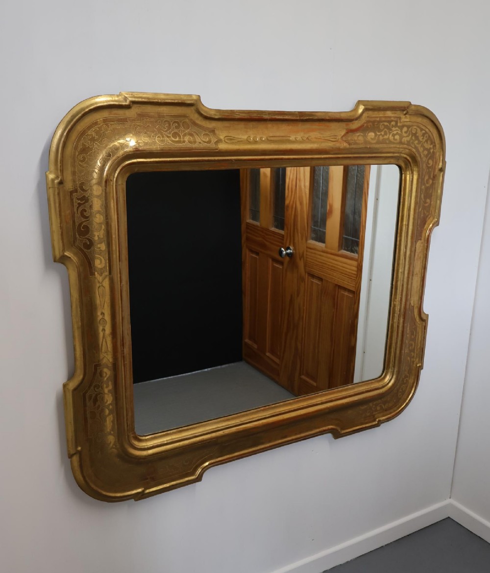 A rectangular 19th-century wall mirror featuring an ornate gold leaf giltwood frame with notched corners and incised scrollwork patterns.