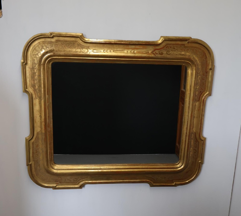 A rectangular 19th-century wall mirror featuring an ornate gold leaf giltwood frame with notched corners and incised scrollwork patterns. View II