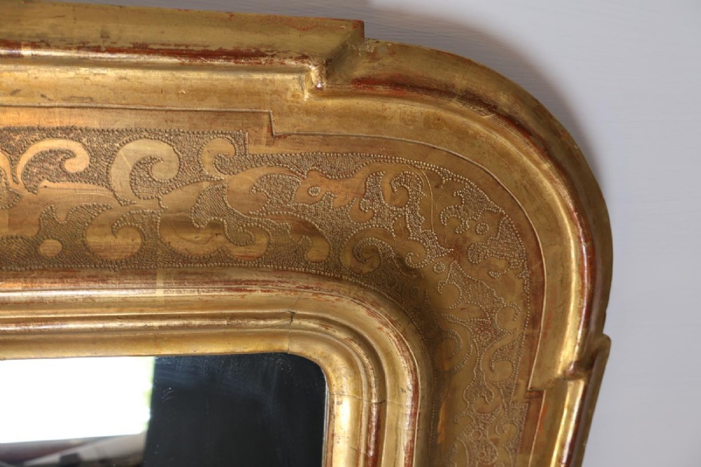 A rectangular 19th-century wall mirror featuring an ornate gold leaf giltwood frame with notched corners and incised scrollwork patterns. View IX