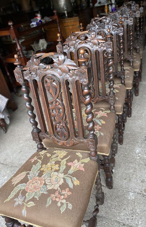 fig 1. A dark carved oak dining chair featuring spiral turned legs, intricate leaf relief carvings on the backrest, and a beige upholstery seat with floral embroidery.
