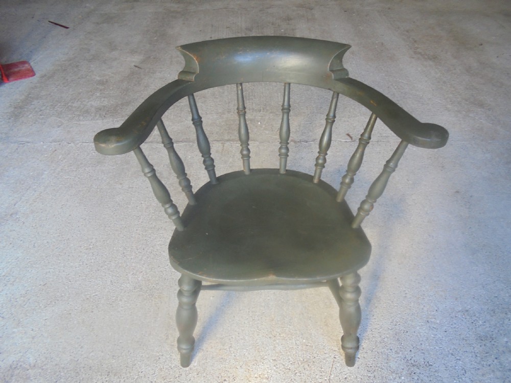 A low-backed wooden captains chair painted in dark green, featuring turned spindles, a curved armrest, and a shaped seat.
